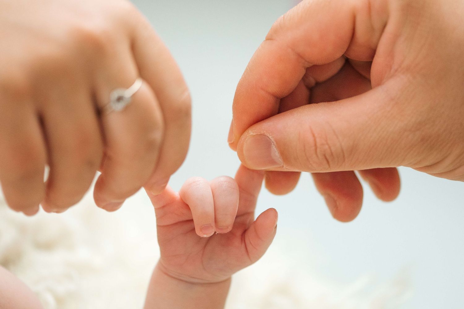A newborn baby grasping an adult's finger, with a mother wearing a diamond ring nearby, symbolizing family love.
