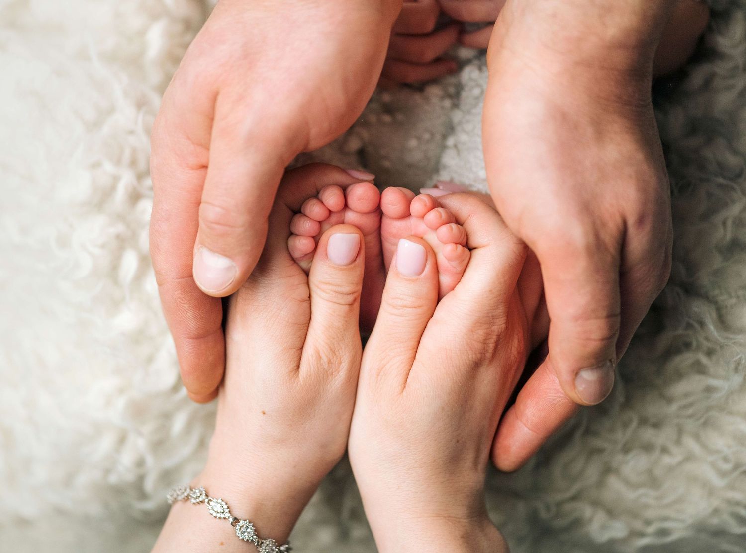 Adult hands gently cradling tiny newborn baby feet, symbolizing love and family bonding on a soft white background.