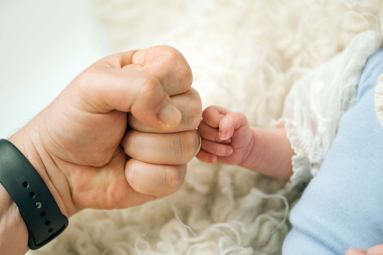 Adult fist bump with a newborn baby's tiny hand, symbolizing father-child bonding moment.