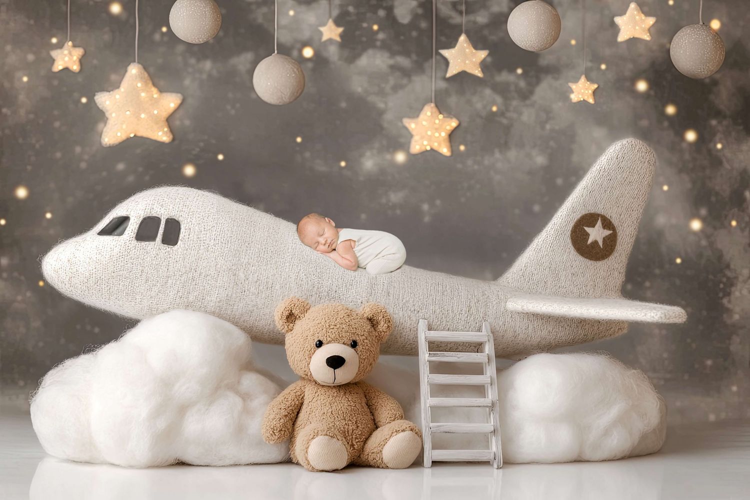 Baby sleeping on a plush airplane prop with a teddy bear, stars, and clouds in a dreamy nursery photo shoot.