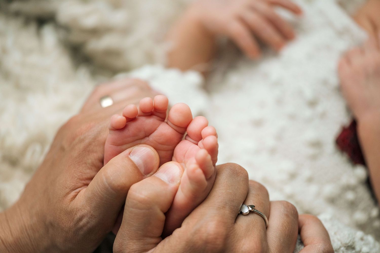 Close-up of adult hands gently cradling tiny newborn baby feet on a soft white blanket.