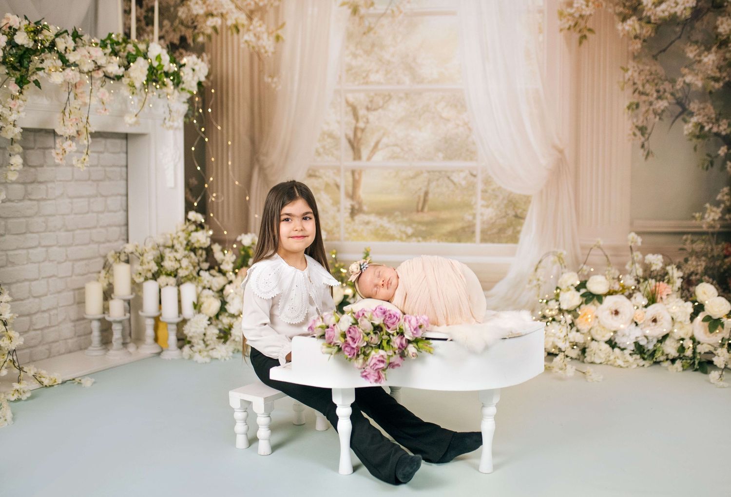 Young girl sits beside a sleeping newborn baby in a white bassinet surrounded by elegant floral decorations.