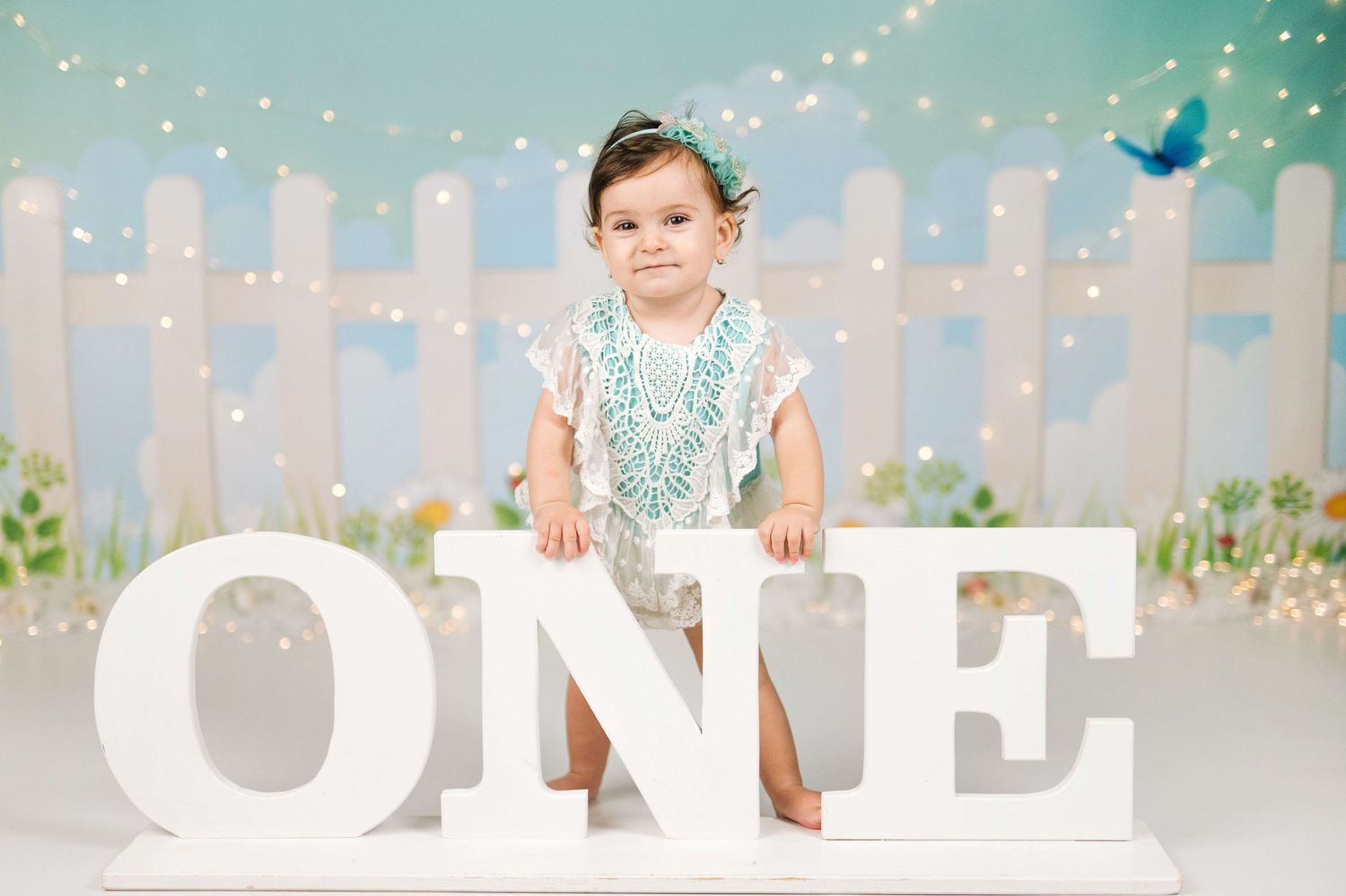 Toddler girl in white dress poses with large ONE letters for first birthday cake smash photo session.