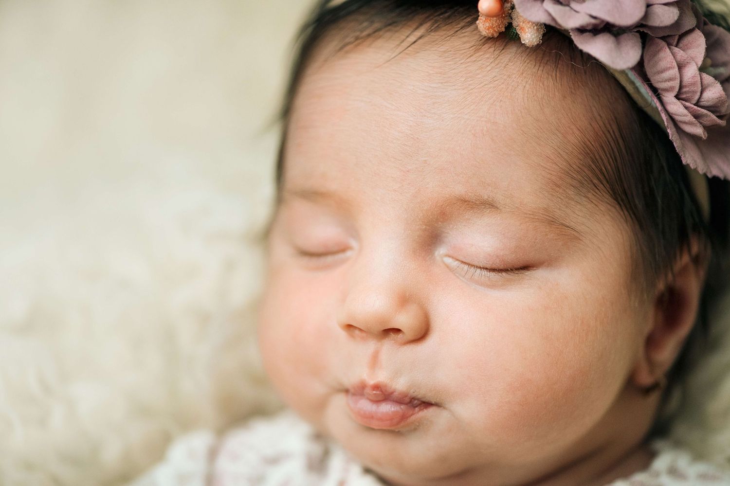 Peaceful sleeping newborn baby girl wearing a floral headband, close-up portrait photography.
