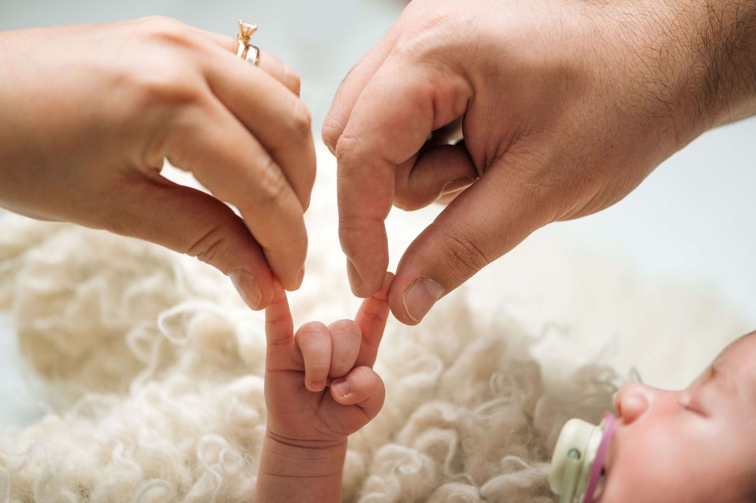 Two parents gently hold their newborn baby's tiny fingers, symbolizing love and new beginnings.