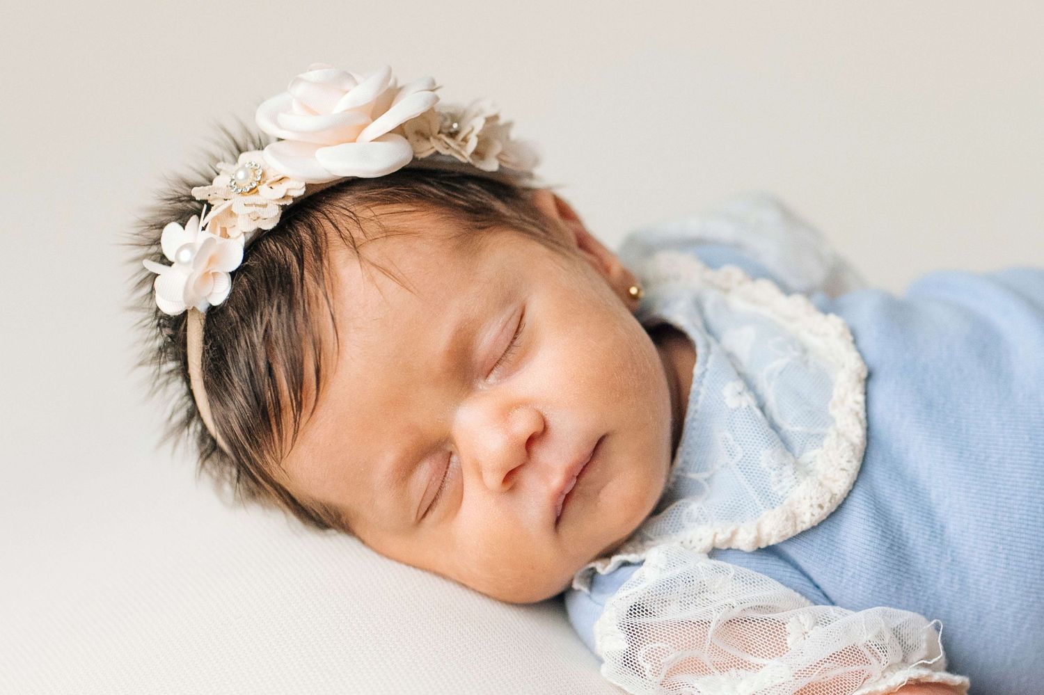 Sleeping newborn baby girl wearing a blue wrap and delicate floral headband with roses.