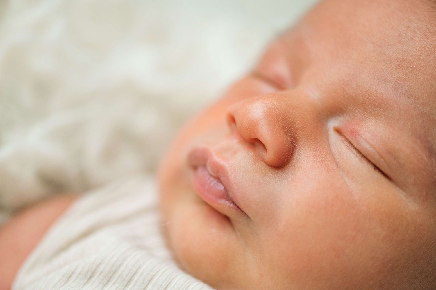 Close-up portrait of a peaceful sleeping newborn baby wrapped in a soft white blanket.