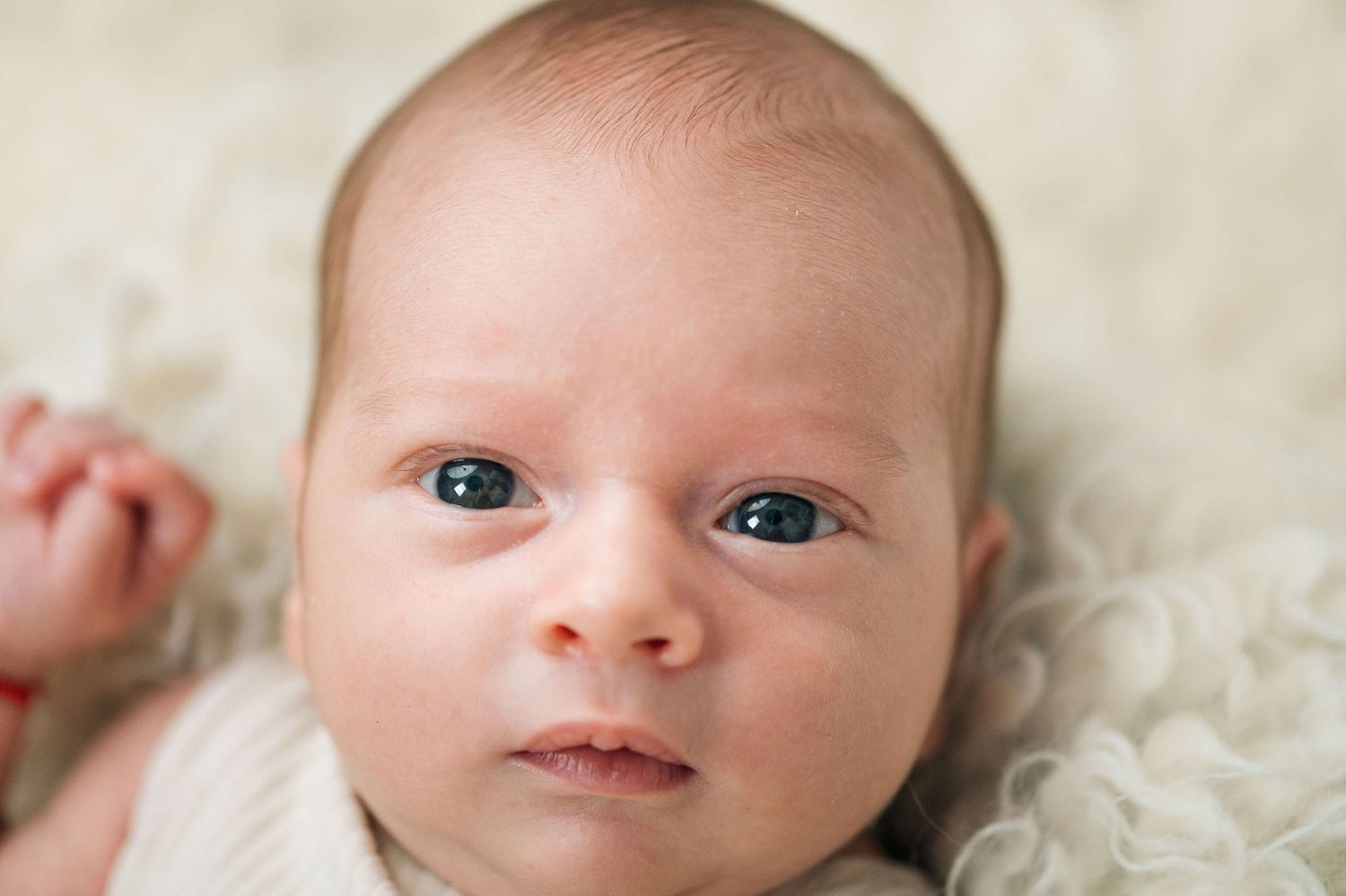 Close-up portrait of a newborn baby with blue eyes lying on a soft white fluffy blanket.