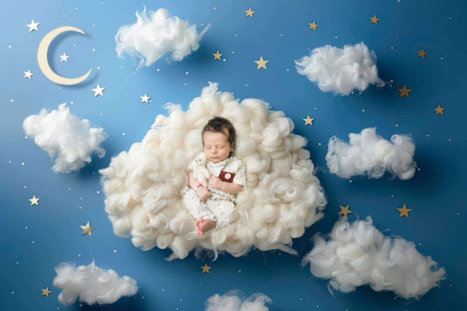 Newborn baby sleeping peacefully on fluffy white clouds with gold stars and crescent moon on blue background.