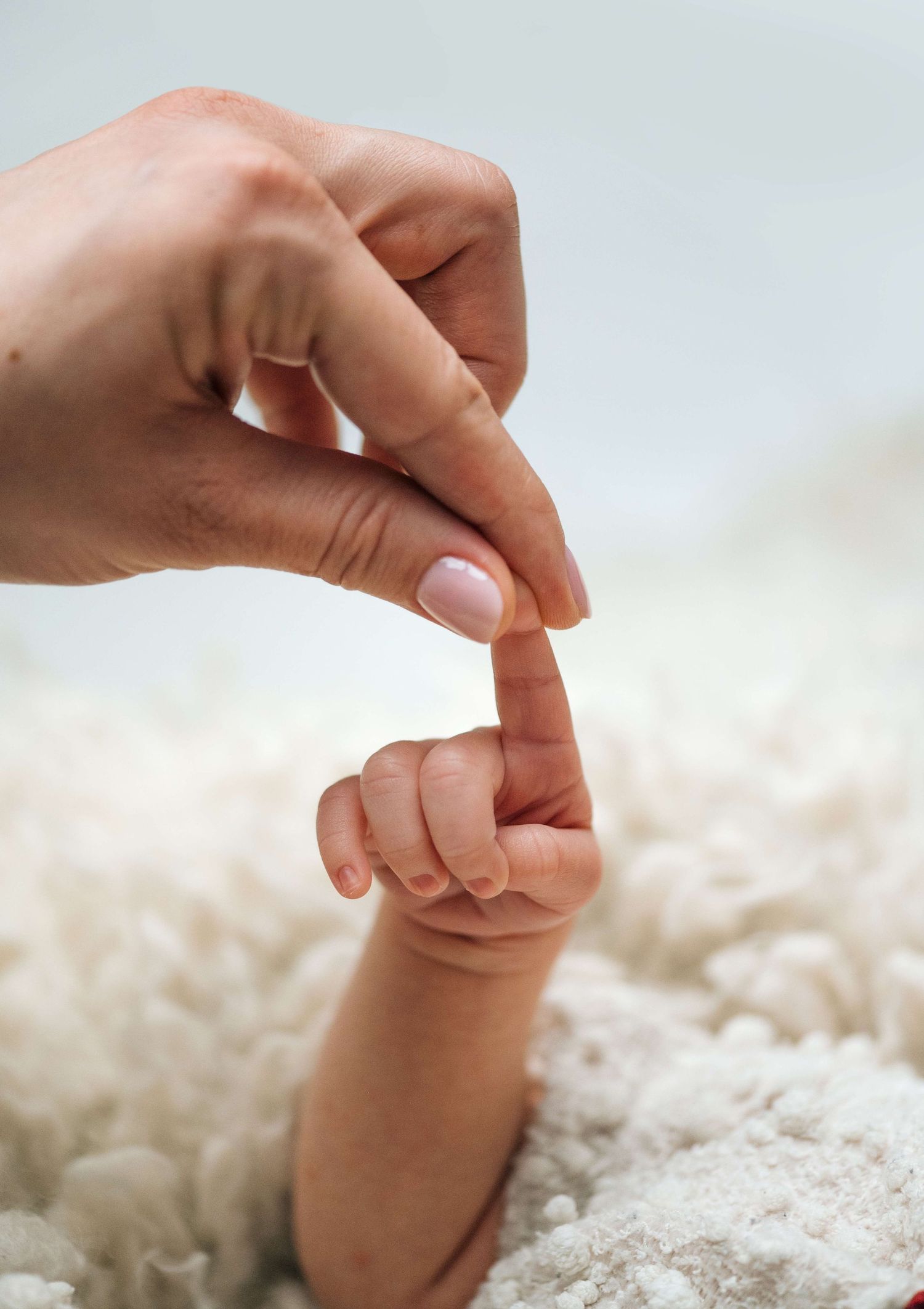 A baby's tiny hand grasping an adult's finger on a soft white blanket, symbolizing newborn love and connection.