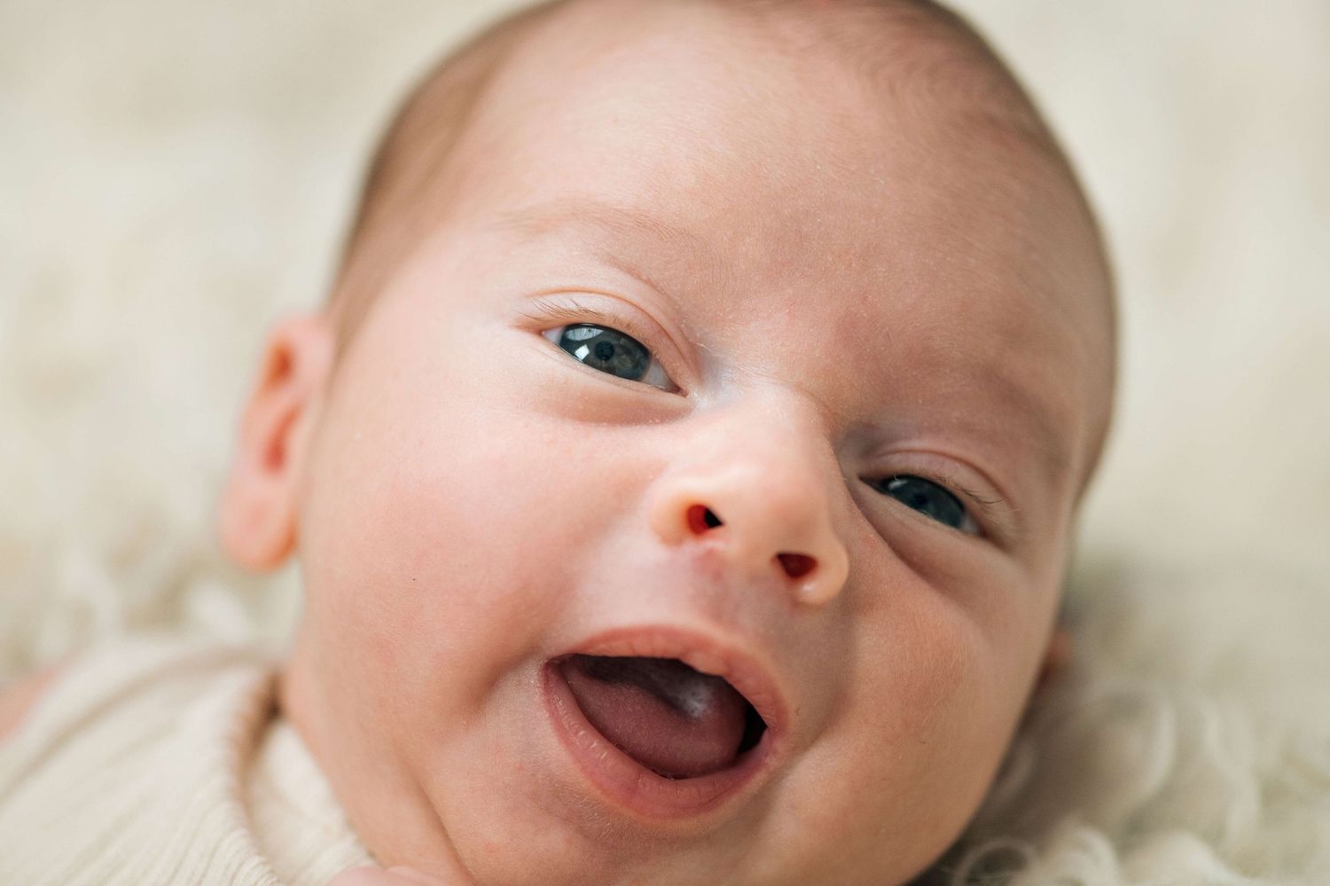 Adorable smiling newborn baby with blue eyes lying on a soft cream blanket in a portrait photo.