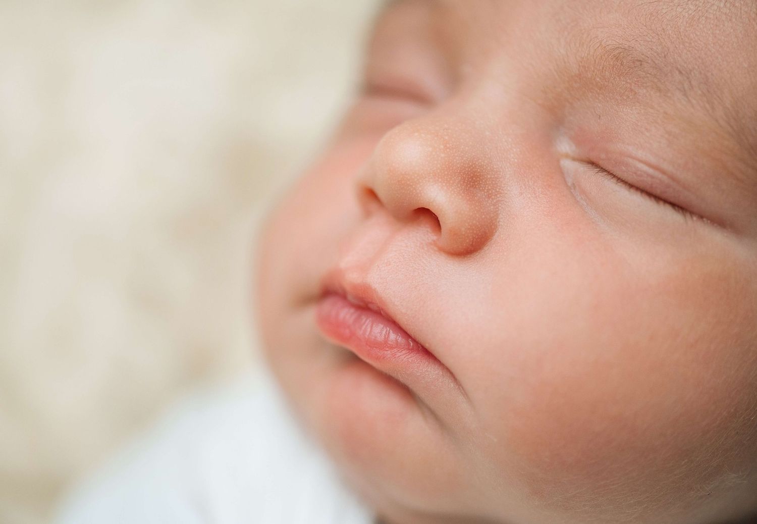 Close-up of a sleeping newborn baby with soft skin and peaceful expression on a white background.