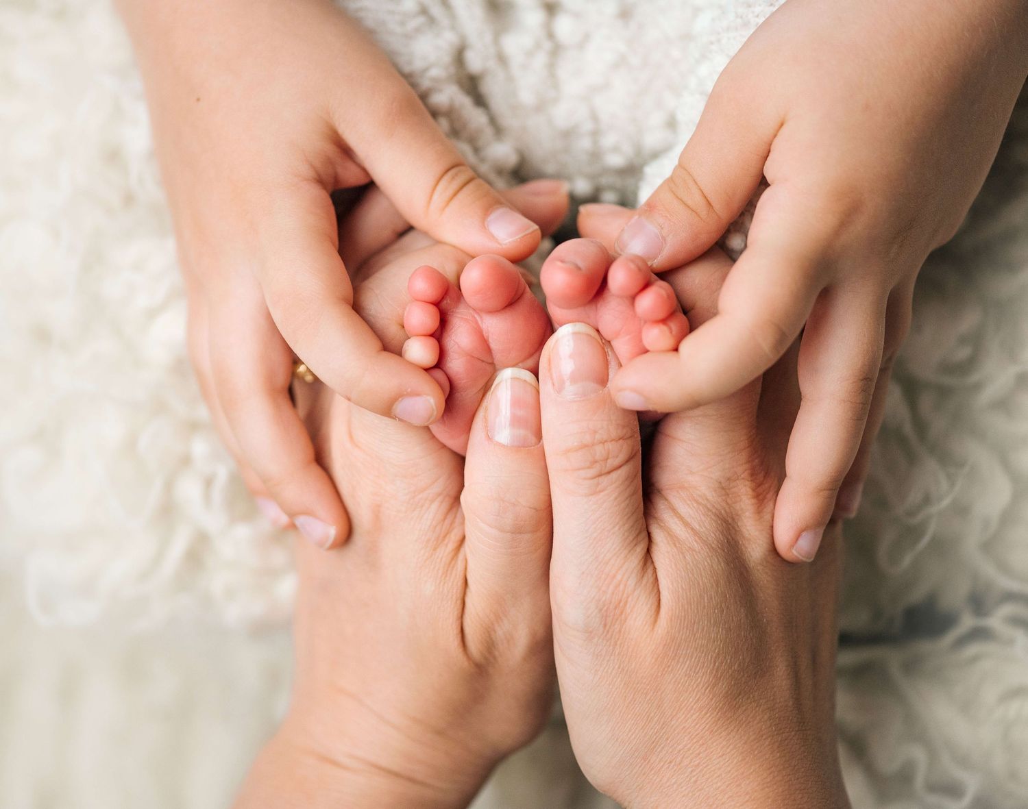 Adult hands gently cradling tiny newborn baby feet, symbolizing love and family bonding.