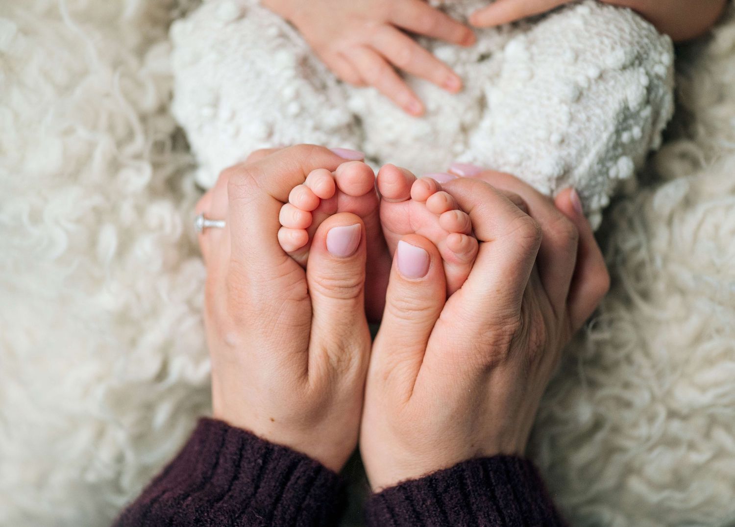 Close-up of adult hands gently cradling tiny newborn baby feet on a soft white blanket.