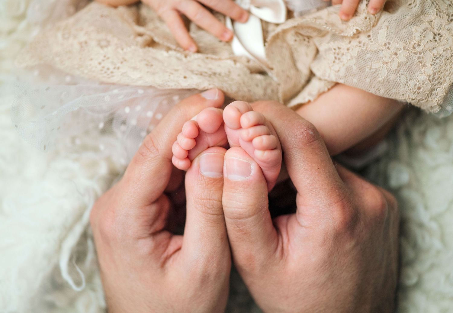 Adult hands gently cradling tiny newborn baby feet in a soft, tender close-up photograph.