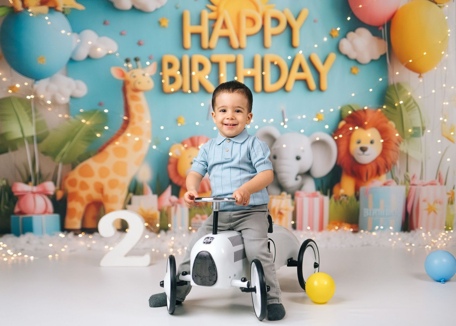 Toddler boy smiling on toy dog ride at a colorful safari-themed 2nd birthday party with Happy Birthday banner.