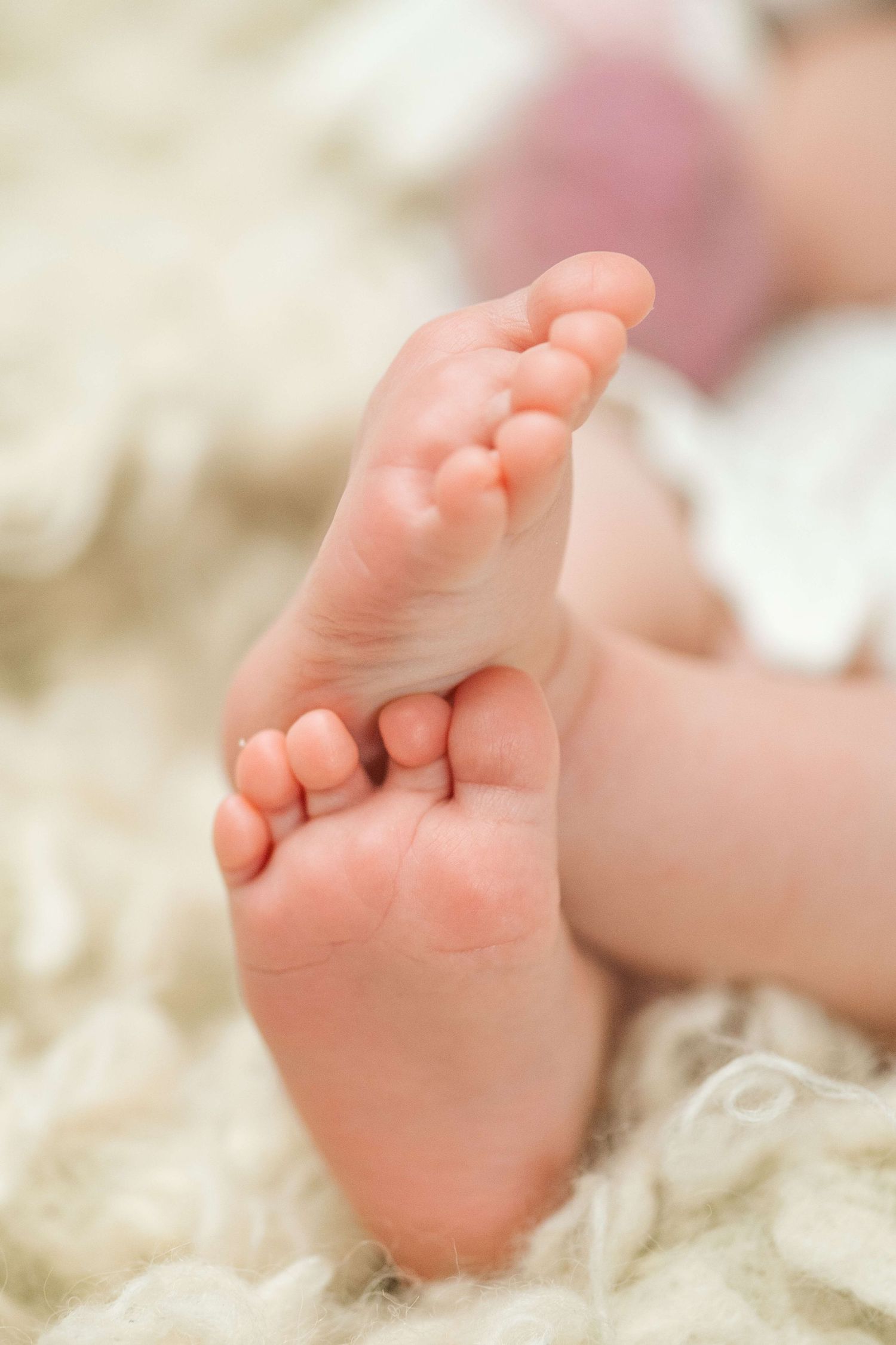 Close-up of tiny newborn baby feet resting on a soft white fluffy blanket.