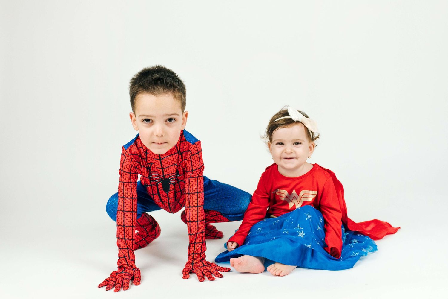Two children in superhero costumes, a boy in Spiderman and a girl in Wonder Woman, posing on a white background.