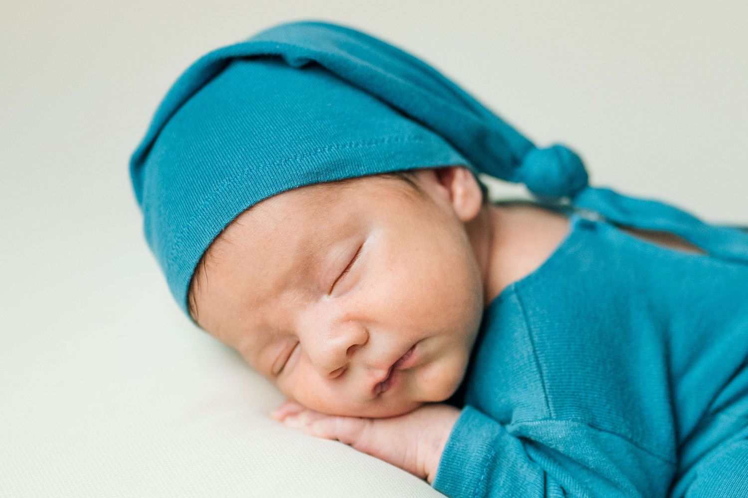 Peaceful newborn baby sleeping in teal outfit and knotted hat, perfect newborn photography pose.