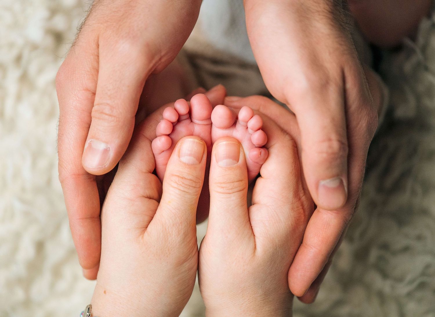 Adult hands gently cradling tiny newborn baby feet, symbolizing family love and new parenthood.