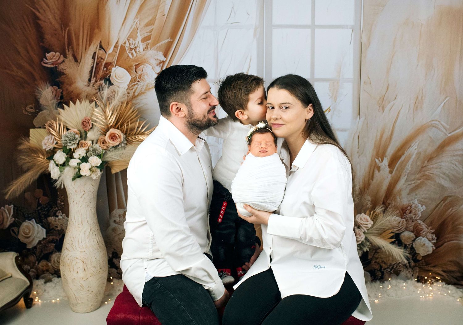 Family portrait with parents and two children, newborn baby, floral backdrop, elegant studio photography.