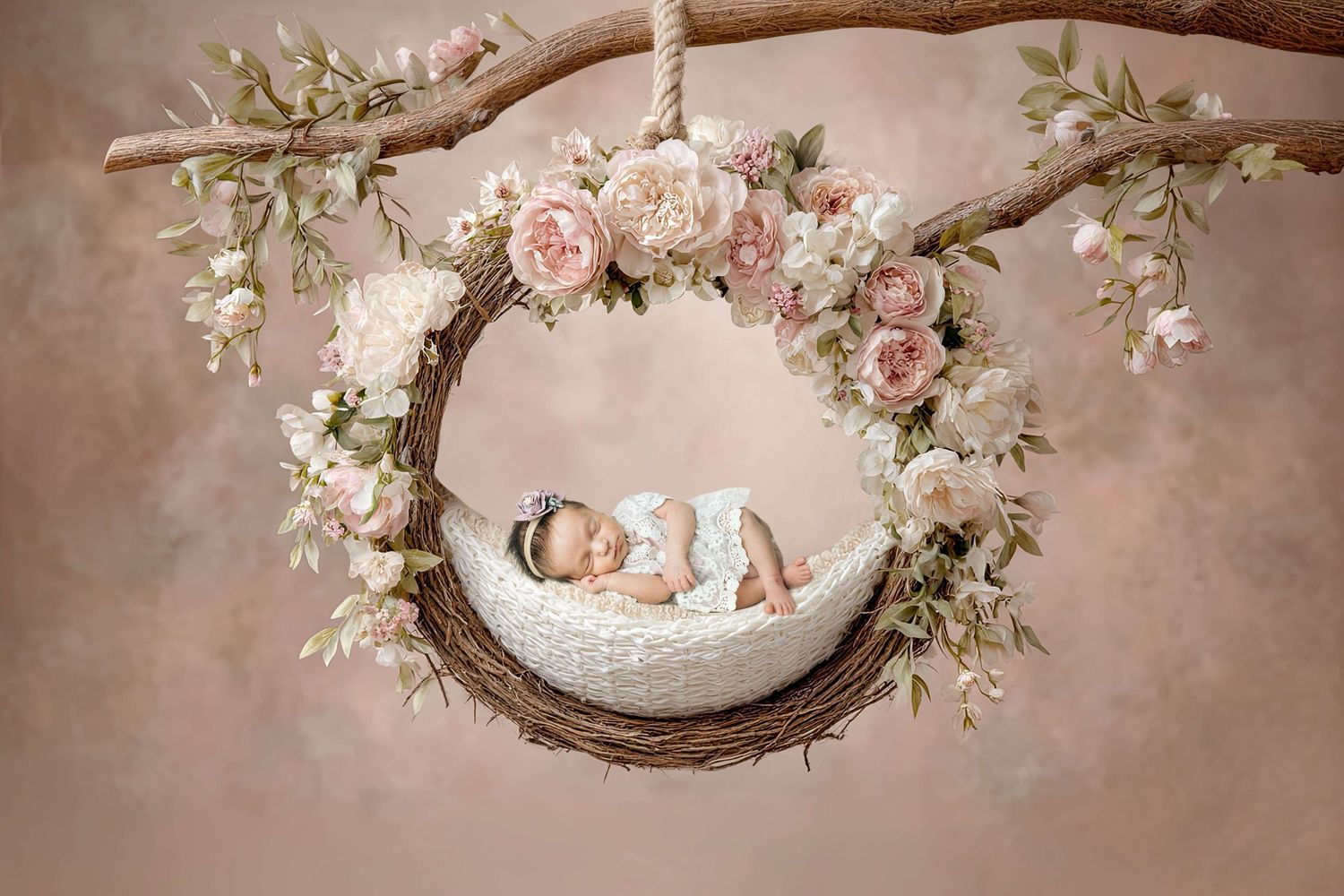 Sleeping newborn baby in a floral wreath swing decorated with pink roses for a professional photo session.