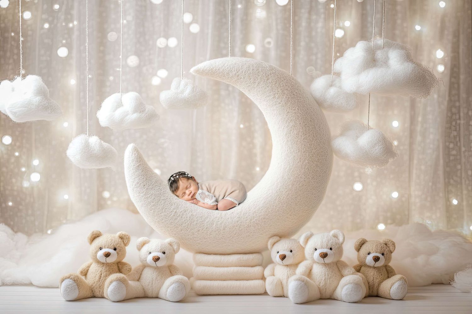Newborn baby sleeping on a white crescent moon prop surrounded by teddy bears and fluffy clouds in a dreamy nursery setting.