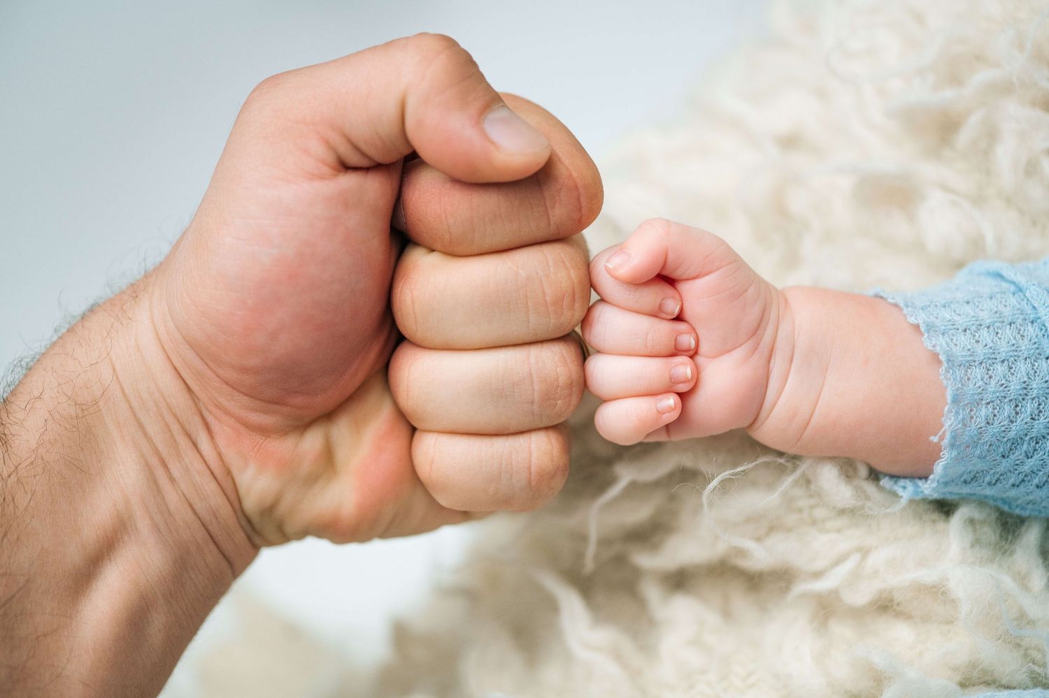 Adult fist bump with tiny newborn baby hand, symbolizing father-child bond and new parenthood.
