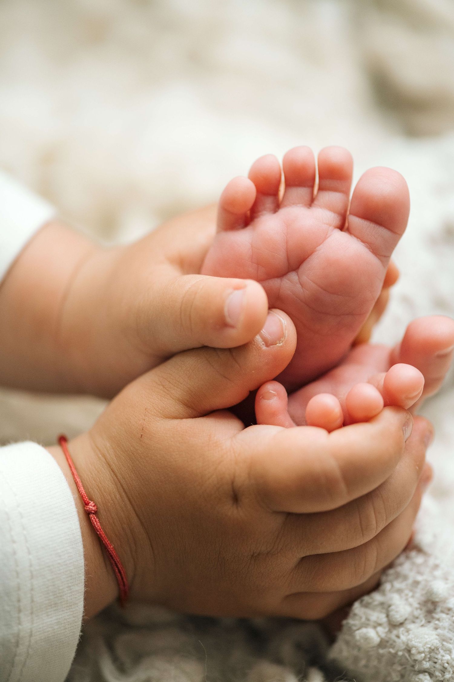 Close-up of gentle hands cradling tiny newborn baby feet, showcasing delicate pink toes and soft skin.