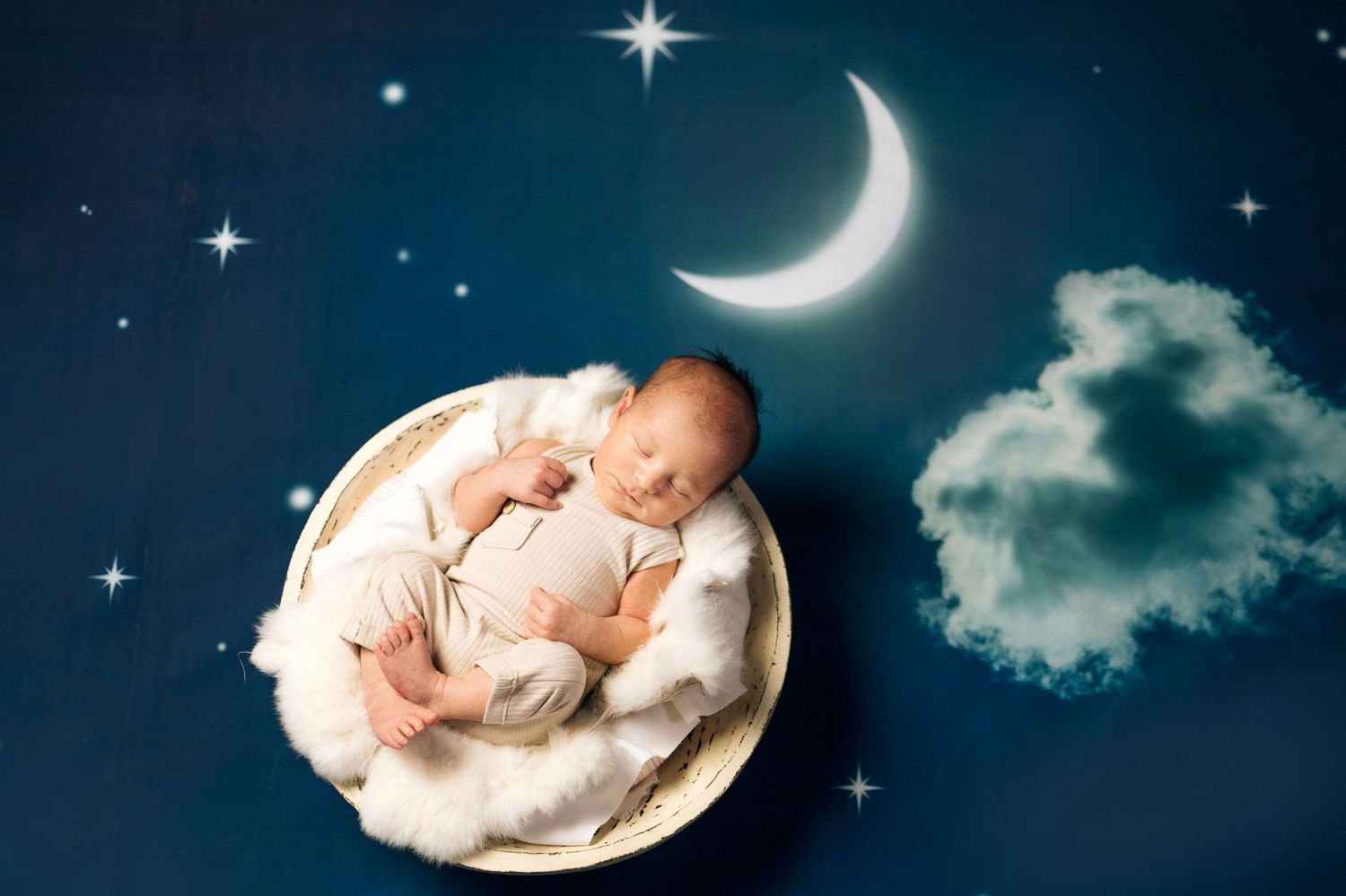 A peaceful newborn baby sleeping in a round basket on a dreamy night sky background with crescent moon and stars.