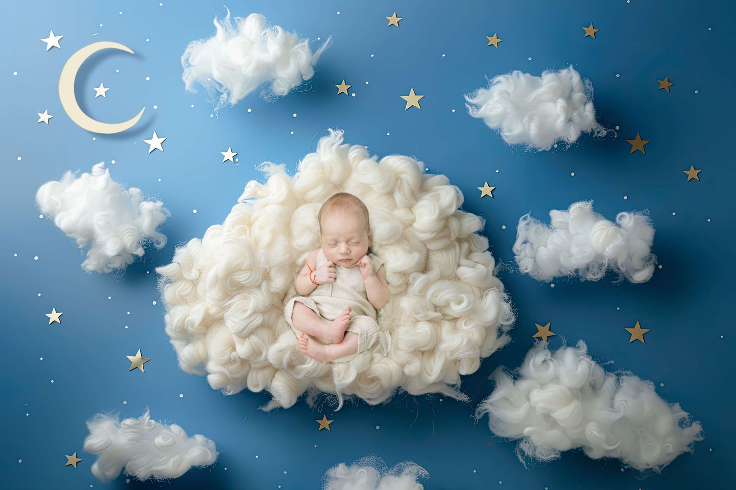 Newborn baby sleeping peacefully on fluffy white clouds with gold stars and crescent moon on blue background.