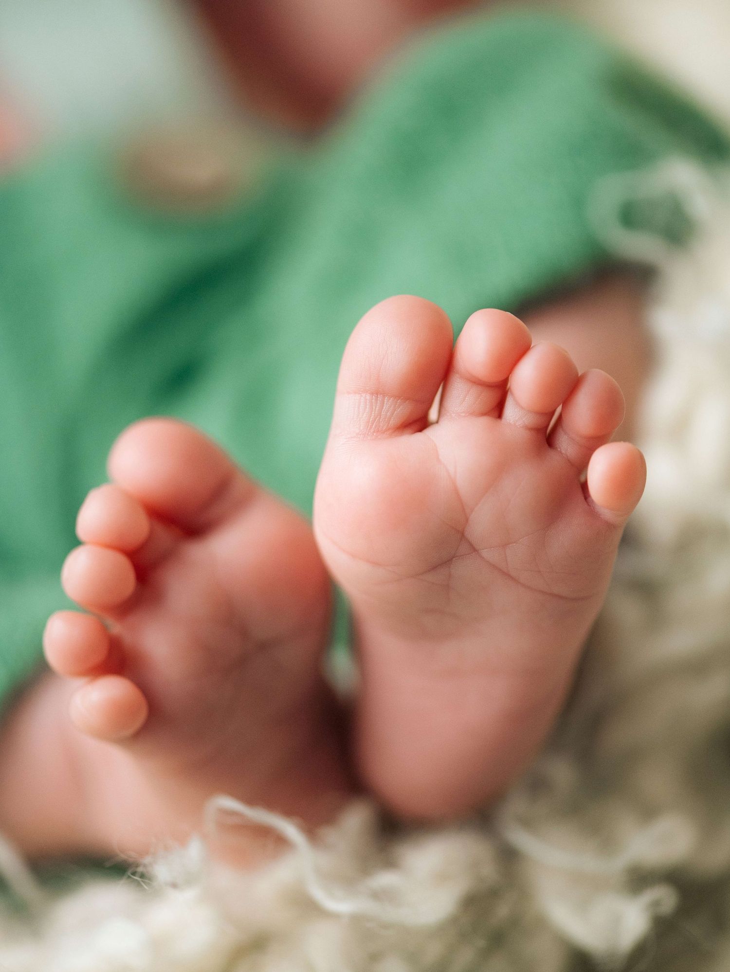 Close-up of tiny newborn baby feet resting on a soft fluffy blanket, wrapped in a green cloth.