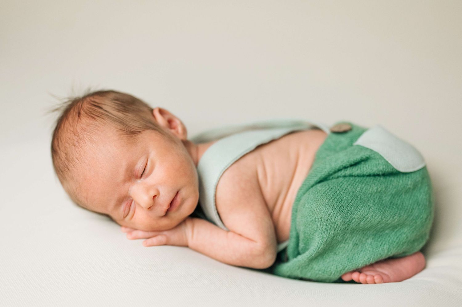 Peaceful newborn baby sleeping wrapped in a green blanket on a white background.