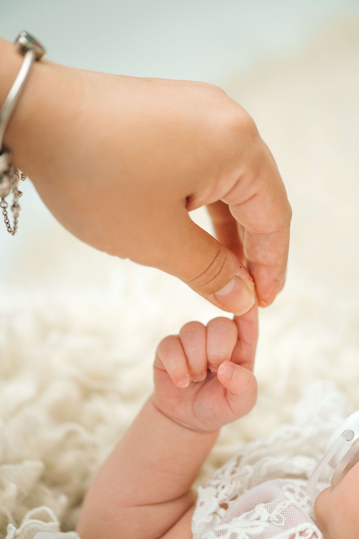 A newborn baby grasping an adult finger, symbolizing the bond between parent and child on a soft white blanket.