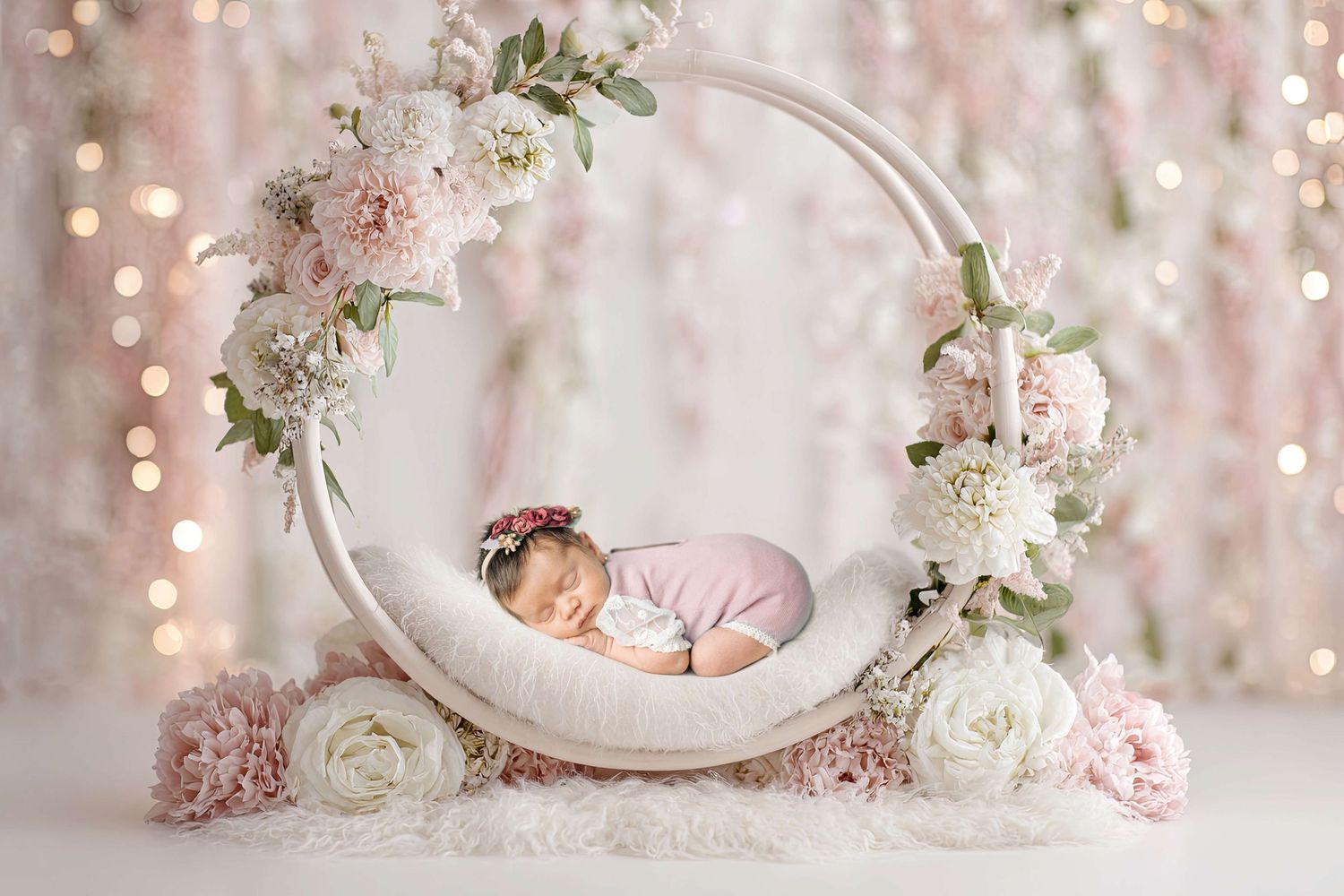 Newborn baby sleeping peacefully in a floral wreath prop with pink and white flowers and soft bokeh lights.