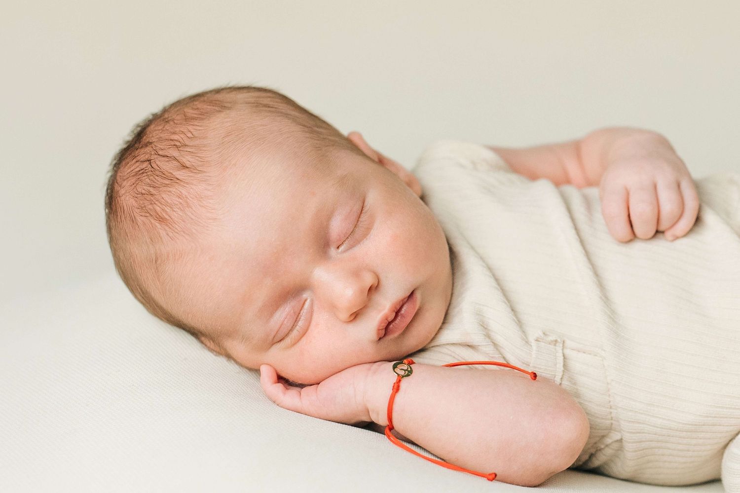 Peaceful newborn baby sleeping wrapped in cream swaddle with red string bracelet on wrist.