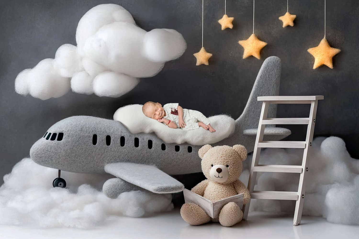 Newborn baby sleeping on a plush airplane prop with teddy bear, clouds, and star decorations in a dreamy nursery photo.