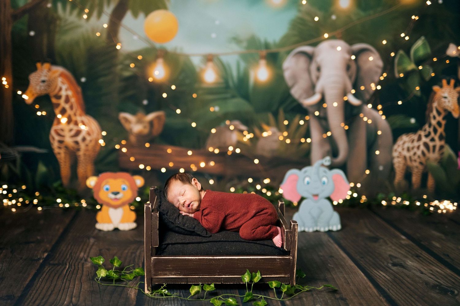 Newborn baby sleeping in a tiny wooden bed surrounded by jungle animal decorations and fairy lights in a safari themed photo.
