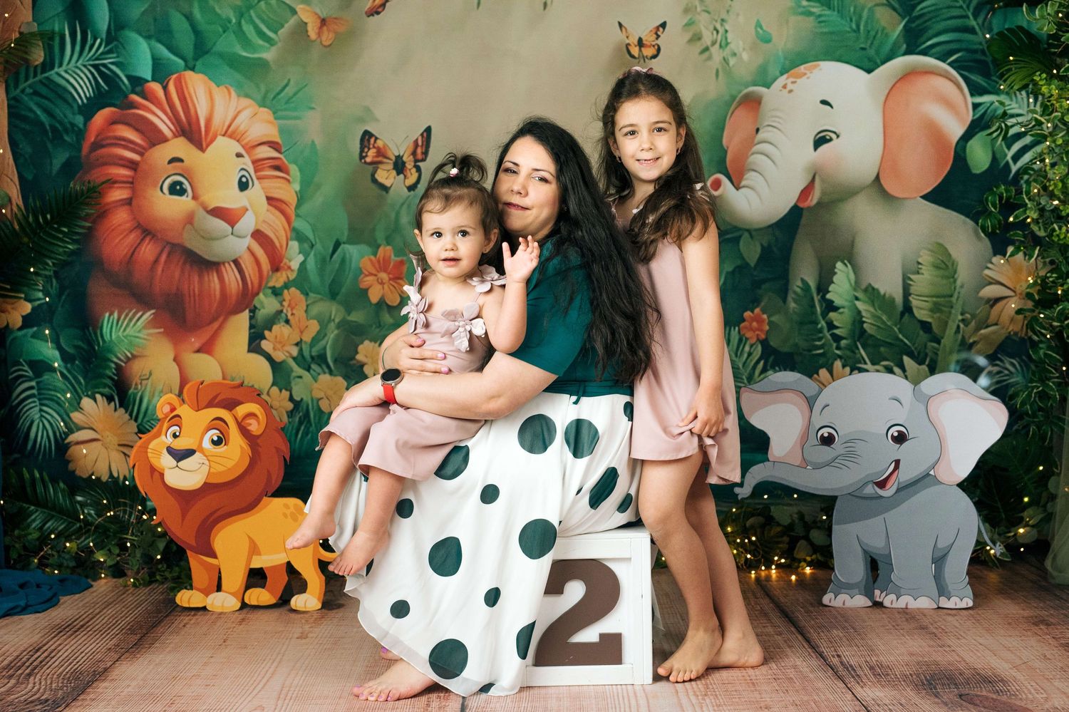 Woman with two girls posing in front of jungle safari backdrop with lion, elephant cartoon characters and number 2 block.
