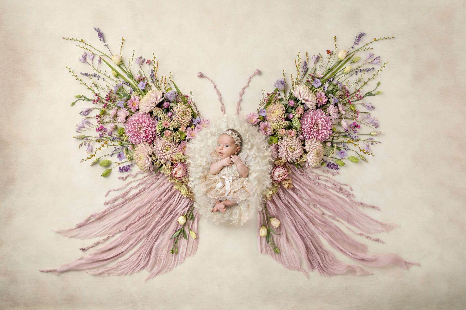 Newborn baby sleeping in butterfly wings made of pink and purple flowers on a soft white background.