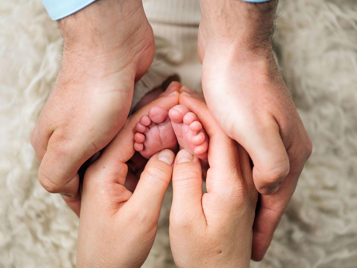 Two adult hands cradling tiny newborn baby feet, symbolizing parental love and new family beginnings.