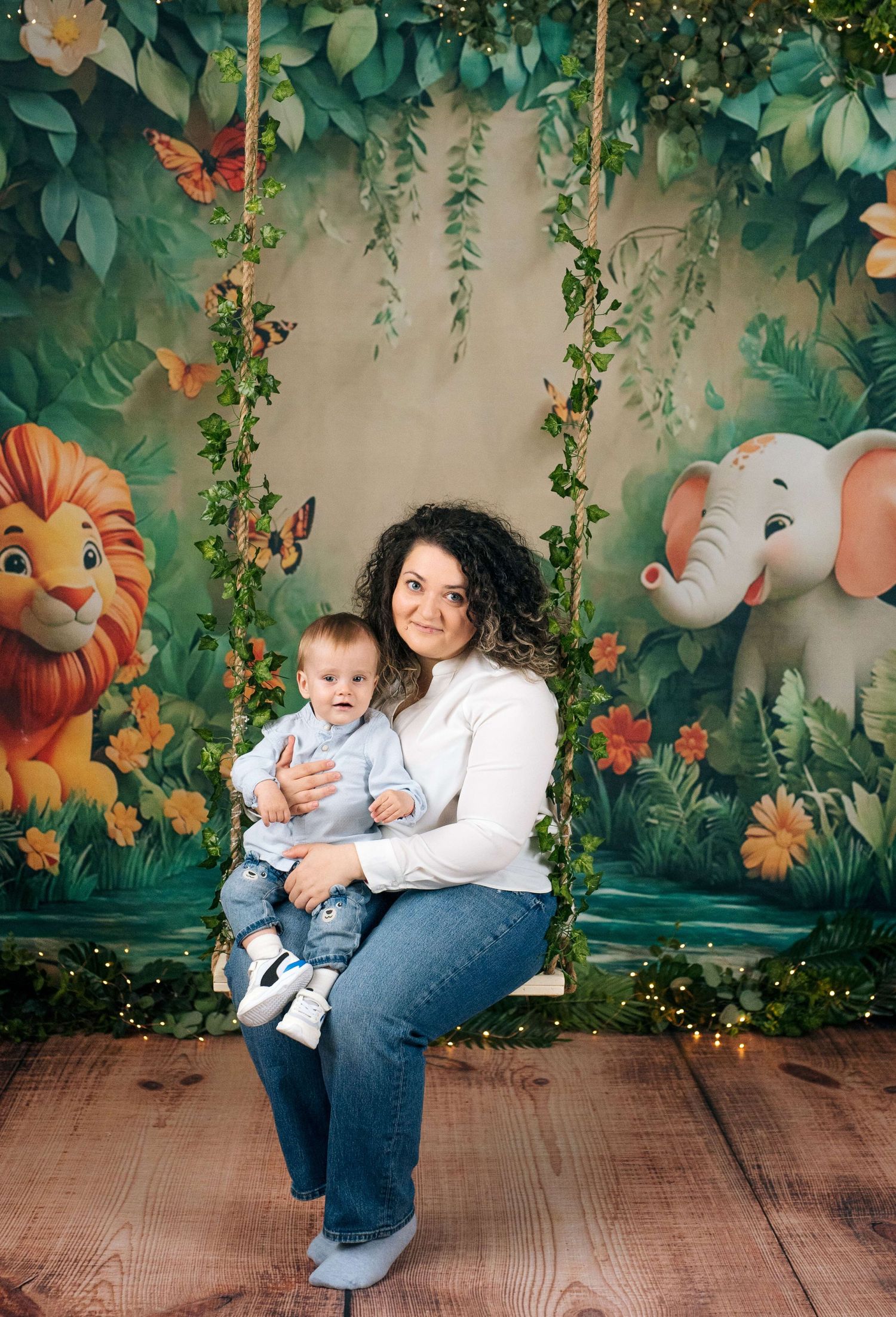 Mother and baby sitting on a swing with a colorful jungle-themed backdrop featuring a lion and elephant.