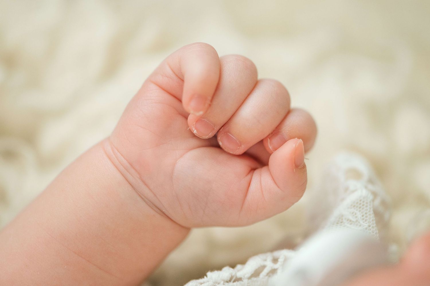 Close-up of a newborn baby's tiny clenched fist resting on a soft white blanket.