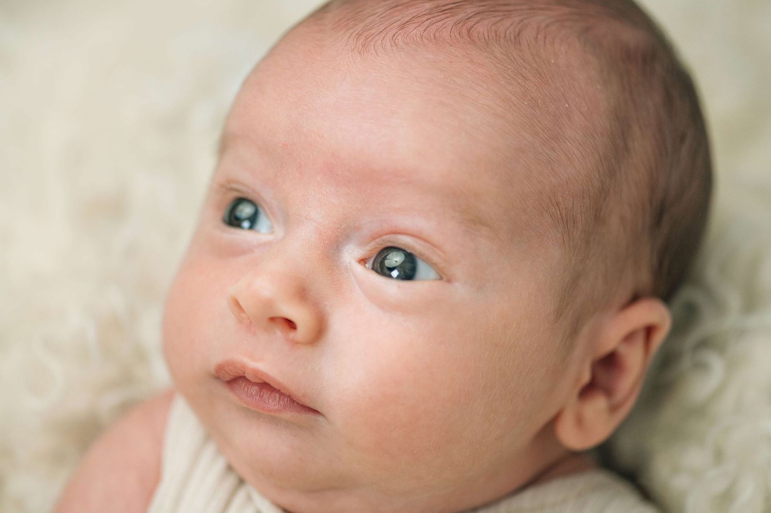 Close-up portrait of a newborn baby with blue eyes lying on a soft white blanket.