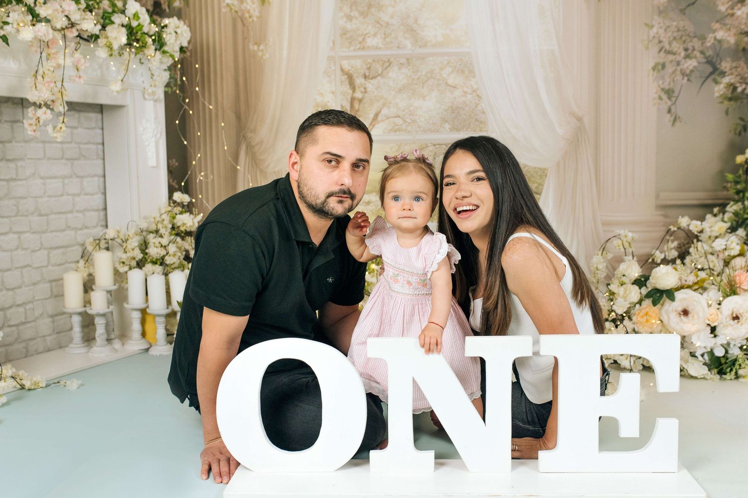 Family celebrating baby's first birthday with ONE letter props and floral backdrop.