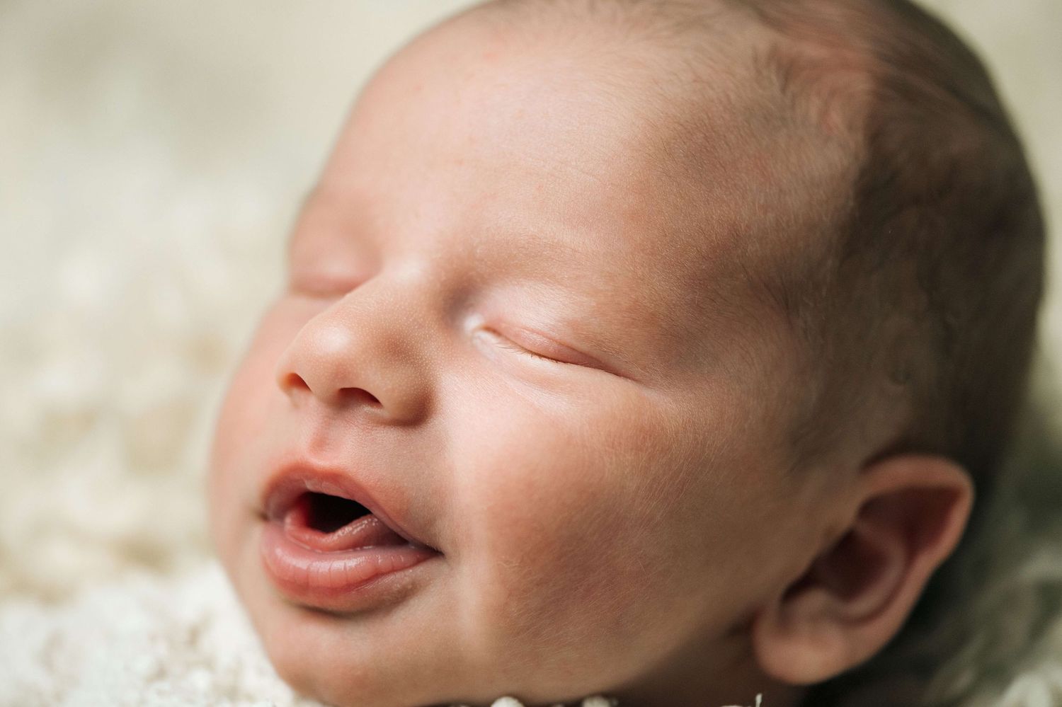 Close-up of a peaceful sleeping newborn baby with mouth slightly open on a soft white blanket.