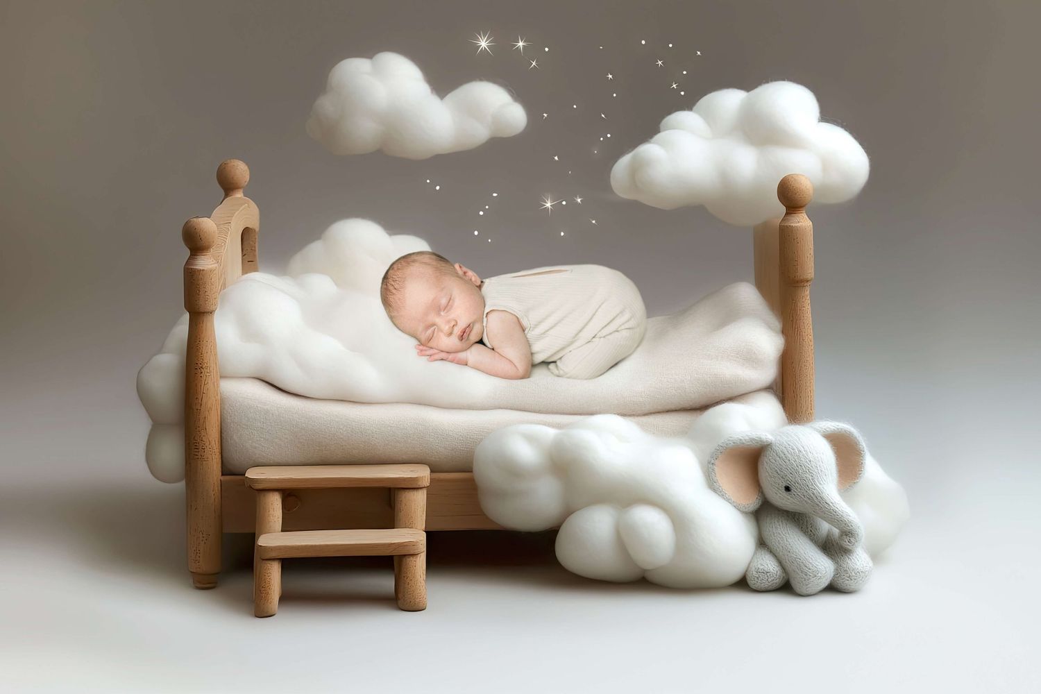 Newborn baby sleeping peacefully on a white fluffy bed with cloud decorations and a toy elephant.