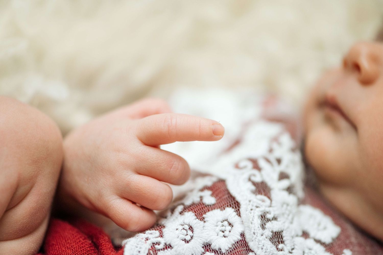 Close-up of a sleeping newborn baby's tiny hand and fingers wearing a delicate white lace outfit.