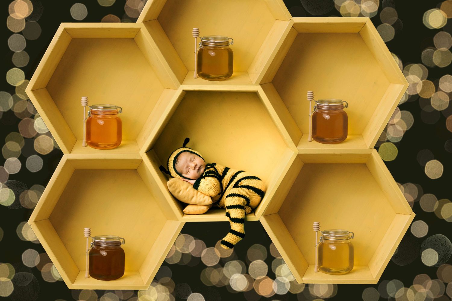 Baby dressed in bee costume sleeping in yellow honeycomb shelf with honey jars and bokeh lights.