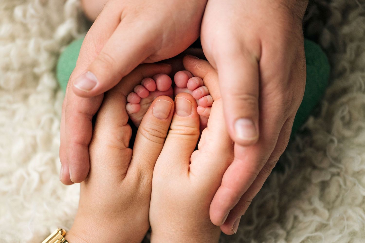 Adult hands gently cradling tiny newborn baby feet, symbolizing parental love and family bonding in a tender moment.